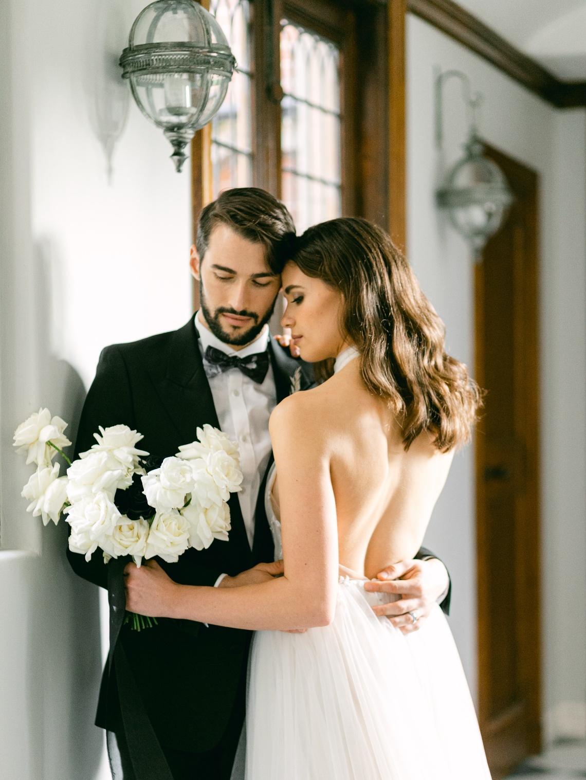 A bride a groom, holding a bouquet of flowers and embracing